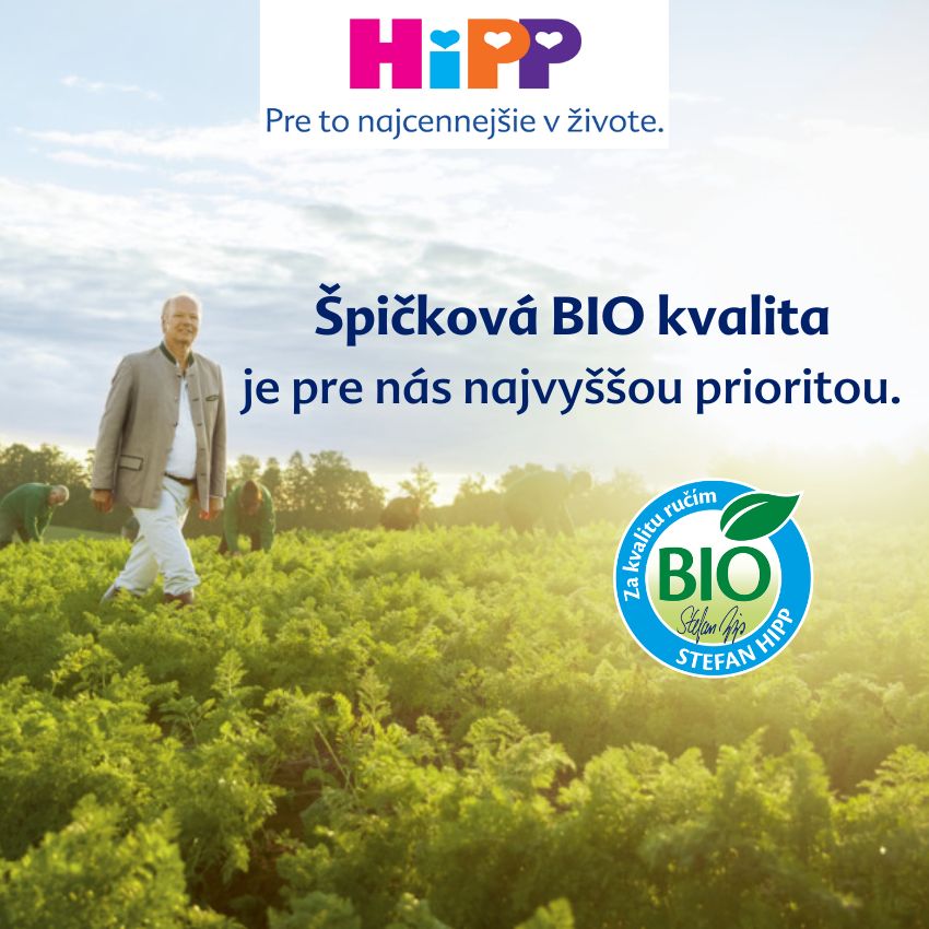 Muž v obleku stojí na poli so skupinou ľudí v pozadí, pod jasnou oblohou, s výrazným logom bio v popredí.