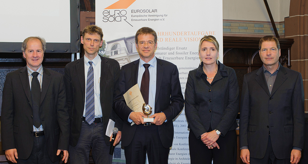 Päť osôb stojí na podujatí pred propagačným bannerom spoločnosti Eurosolar a jedna z nich drží trofej a certifikát.